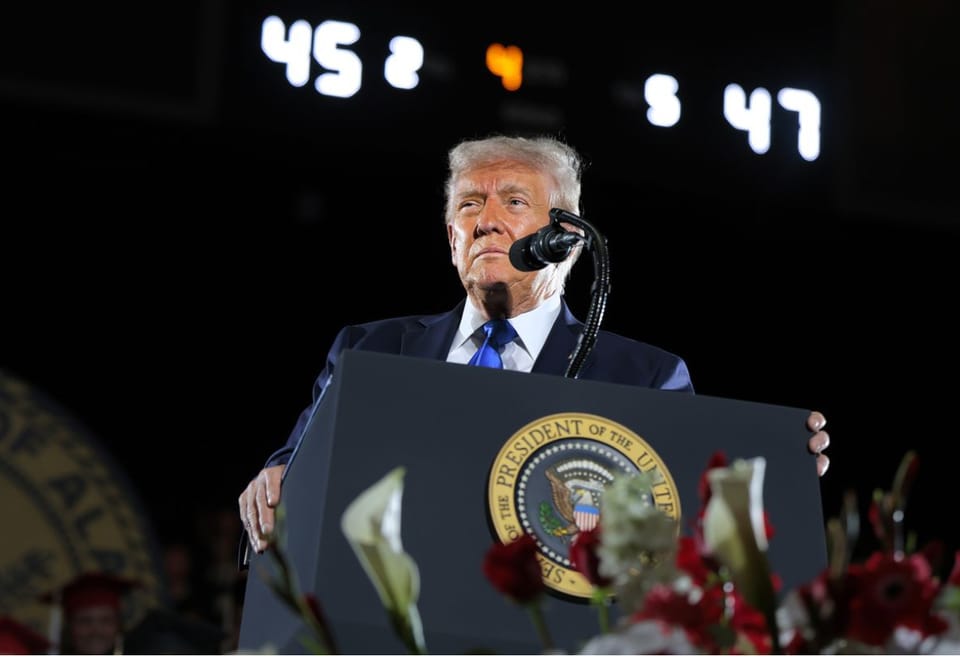 Trump standing at the podium at the University of Alabama with the numbers 45 and 47 behind him.